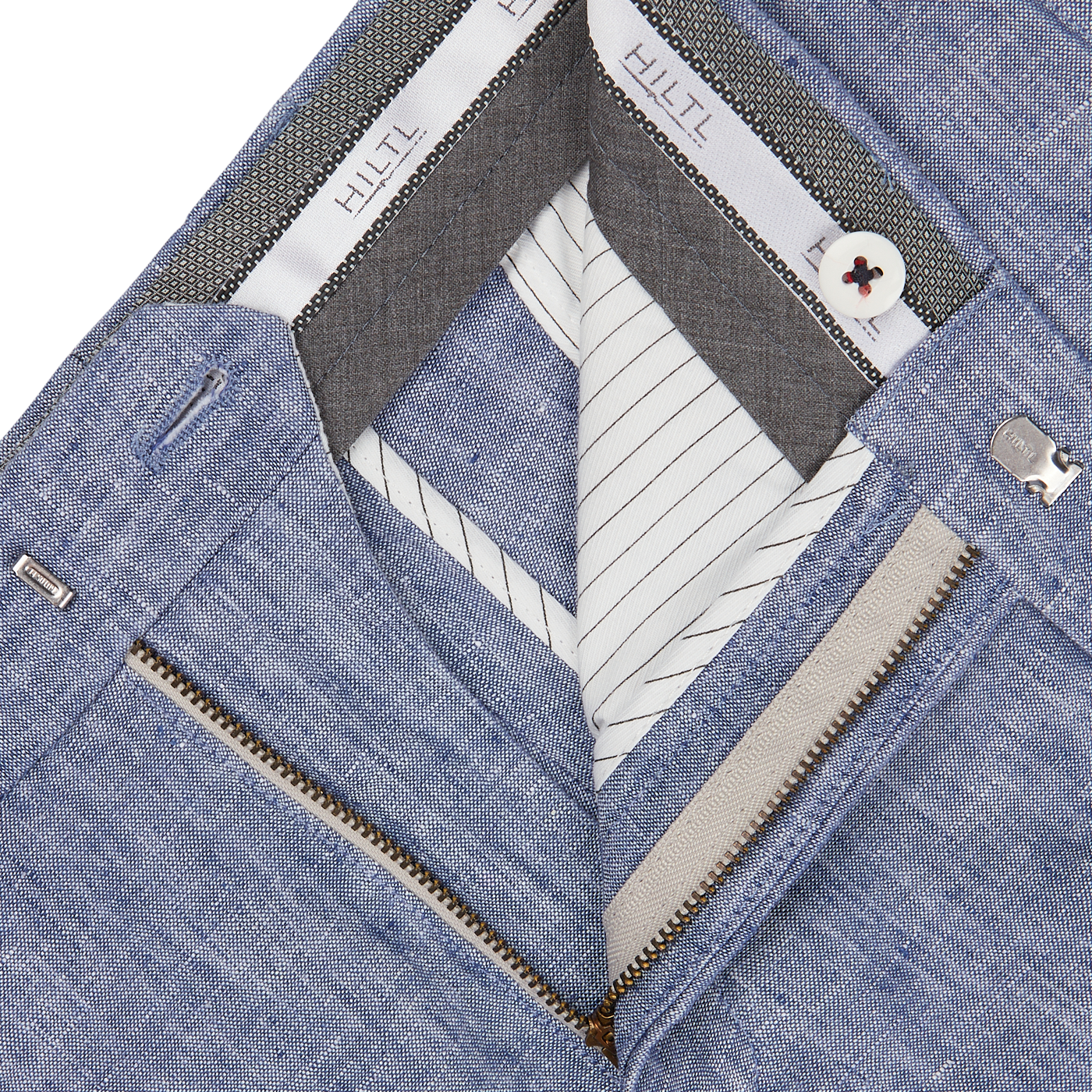 Close-up of an open blue denim jacket showing the inner Hiltl Light Blue Washed Linen Regular Fit Chinos lining, a label, and a partially zipped white inner layer.