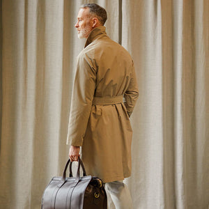A man wearing a Tagliatore khaki beige cotton nylon trench coat and carrying a brown bag.
