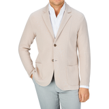 Man in a Maurizio Baldassari light beige silk cotton knitted Milano blazer and light grey pants with a white shirt unbuttoned at the collar, offering a casual substitute to formal wear.