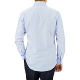 A man seen from behind, wearing a light blue Mazzarelli Light Blue Slim Cutaway Herringbone Shirt and dark trousers, standing against a grey background.