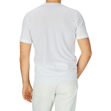 Rear view of a man wearing a Mazzarelli Off-White Merino Wool T-Shirt and light beige pants, standing against a light gray background.