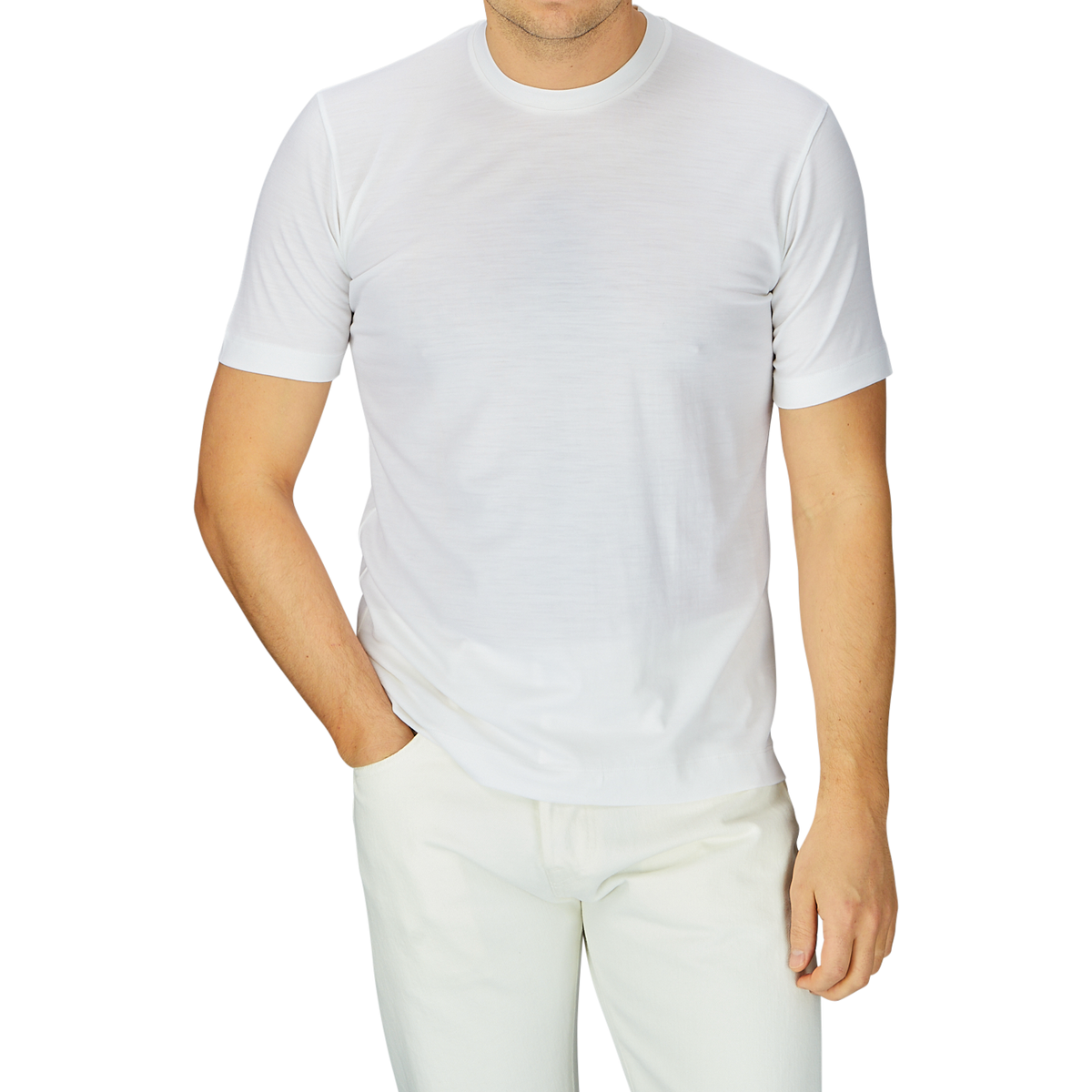 Man in a breathable Off-White Merino Wool T-shirt from Mazzarelli and light beige pants, standing with one hand partially in his pocket against a grey background.