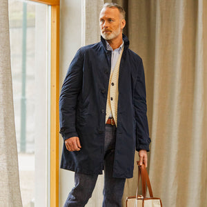 A man in smart casual attire with an Aspesi Navy Blue Micro Nylon Limone Coat, beige sweater, and carrying a brown leather bag.