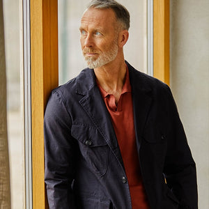 A man in a Navy Blue Ripstop Cotton Bush Jacket by Manifattura Ceccarelli leaning against a window.