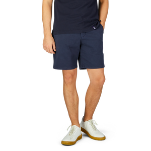 Man wearing Navy Blue Cotton Blend Phillips Shorts by Paige and white sneakers with yellow soles against a neutral background.