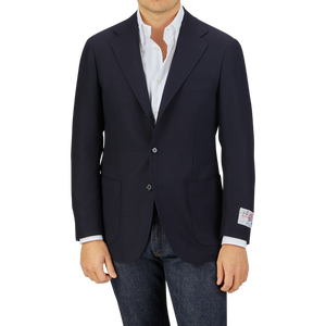 Man wearing a Ring Jacket Navy Blue Wool Balloon Travel Blazer over a white shirt paired with jeans, standing against a gray background.