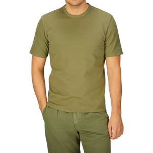A person wearing a plain Olive Green Heavy Organic Cotton T-Shirt by Tela Genova and matching pants against a blue background.