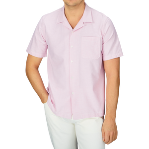 A man wearing a Universal Works Pink Cotton Oxford Camp Collar Road Shirt with white pants.
