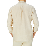 A person seen from behind wearing a Light Beige Washed Linen Legacy Shirt by Xacus, with a cut-away collar, long sleeves, and pleat detail.