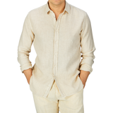 Man wearing a Light Beige Washed Linen Legacy Shirt by Xacus with a cut-away collar and matching pants against a grey background.