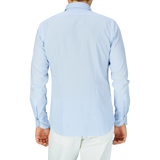 A man standing with his back to the camera, wearing a Xacus Light Blue Cotton Twill Tailor Fit Shirt and white pants.