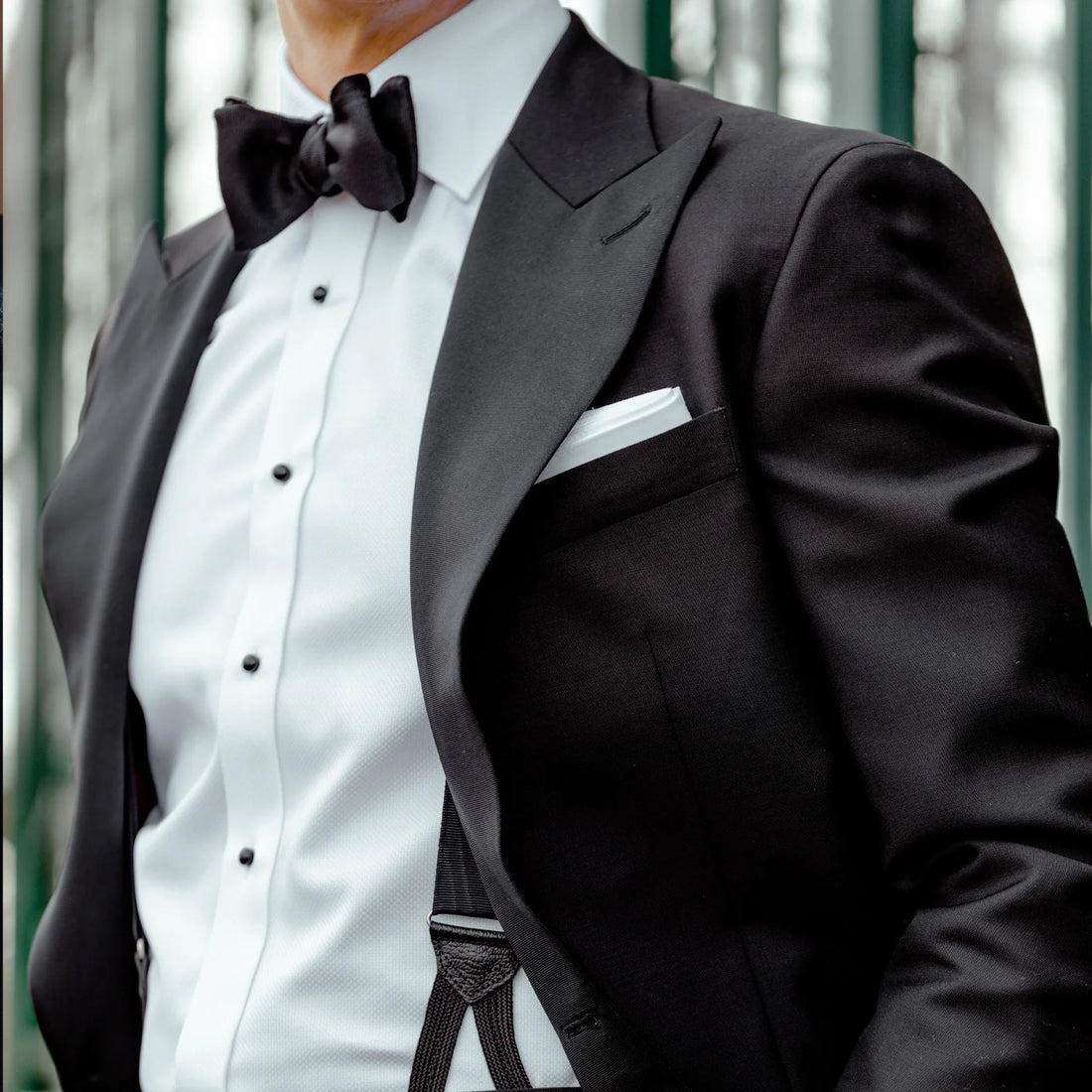 A person wearing a formal black suit with a bow tie and a white pocket square.