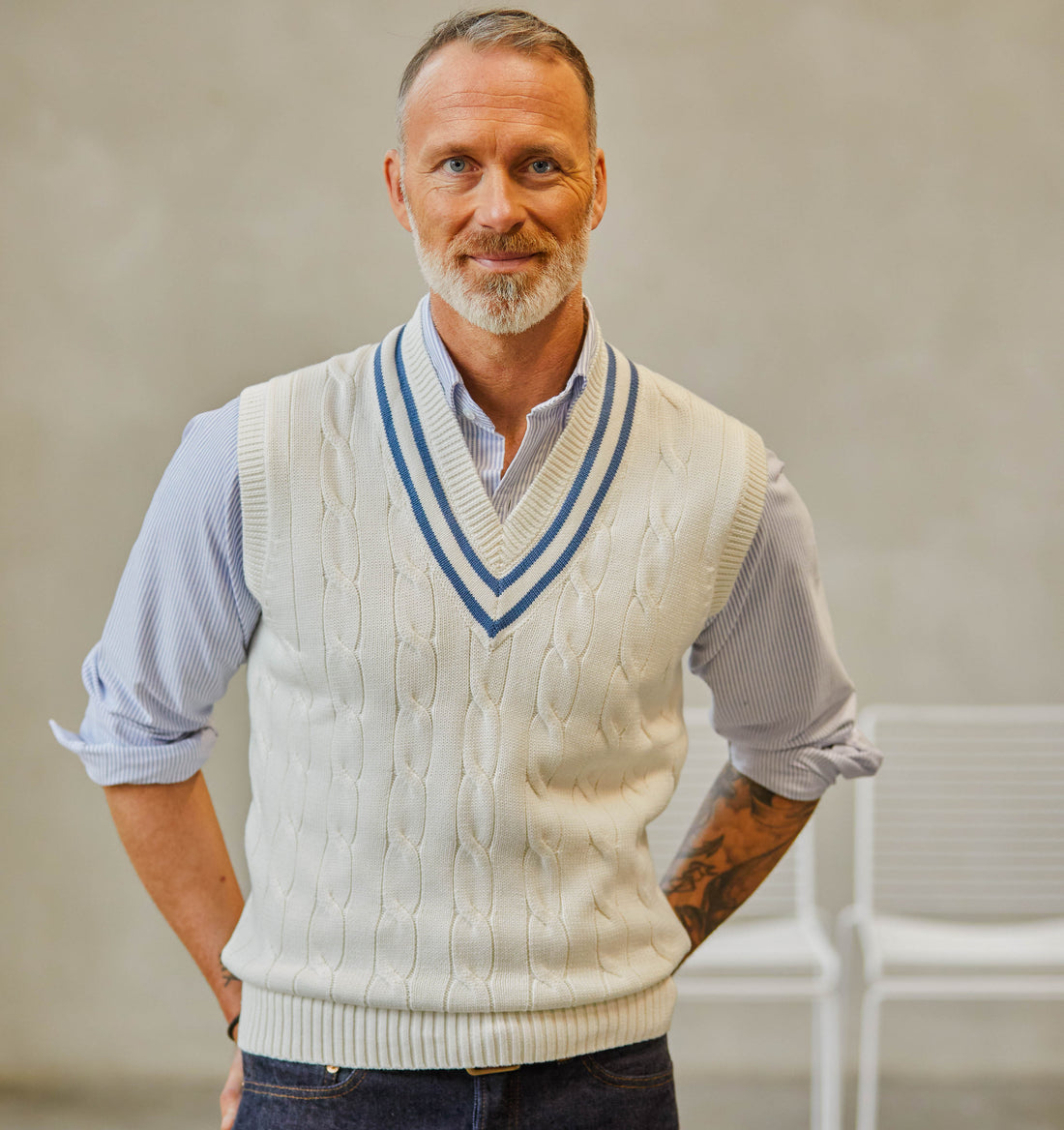 Middle-aged man with a beard, wearing a white cable-knit sweater vest, posing in a studio with a neutral background.