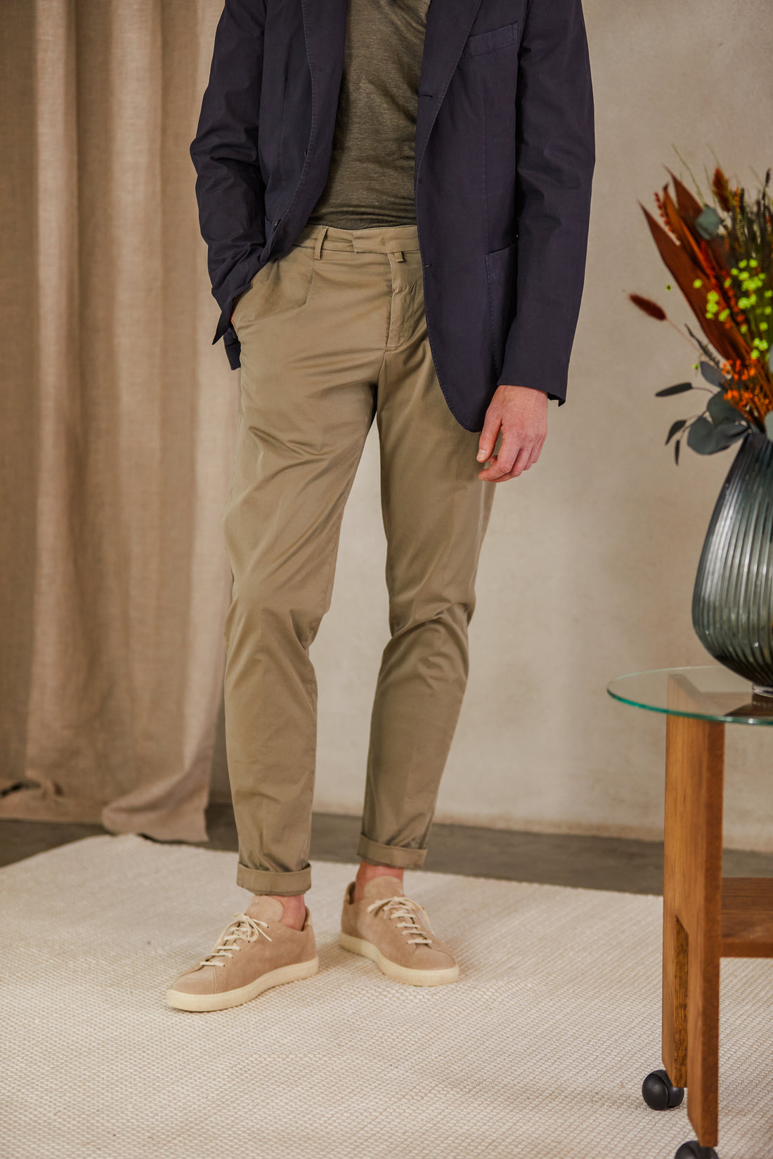 Man standing in casual attire featuring khaki trousers, a green t-shirt, and a navy blazer, complemented by beige sneakers.