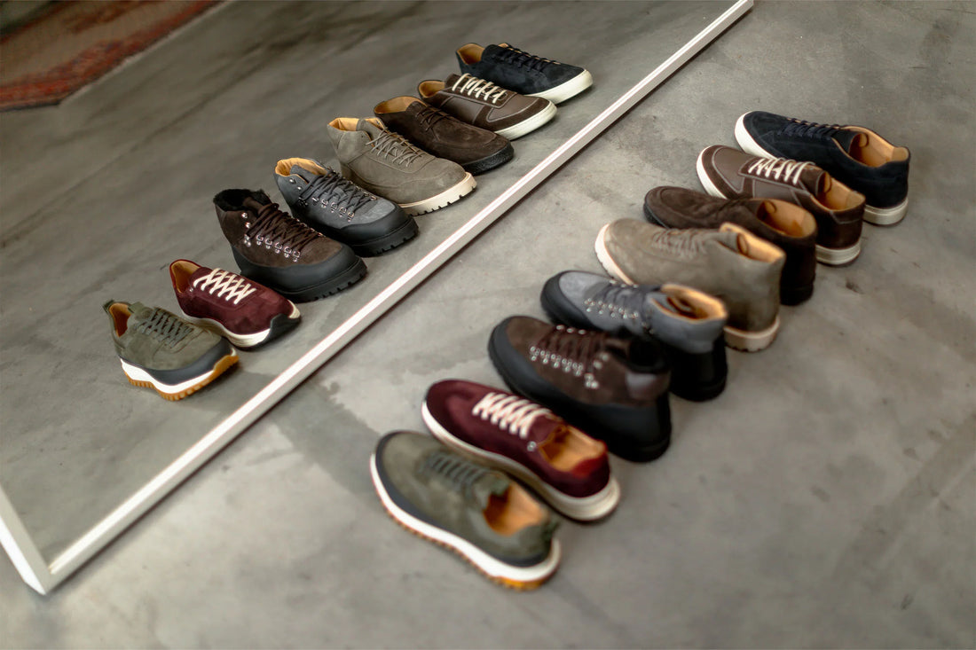 A collection of various shoes neatly aligned next to a mirror on a concrete floor.