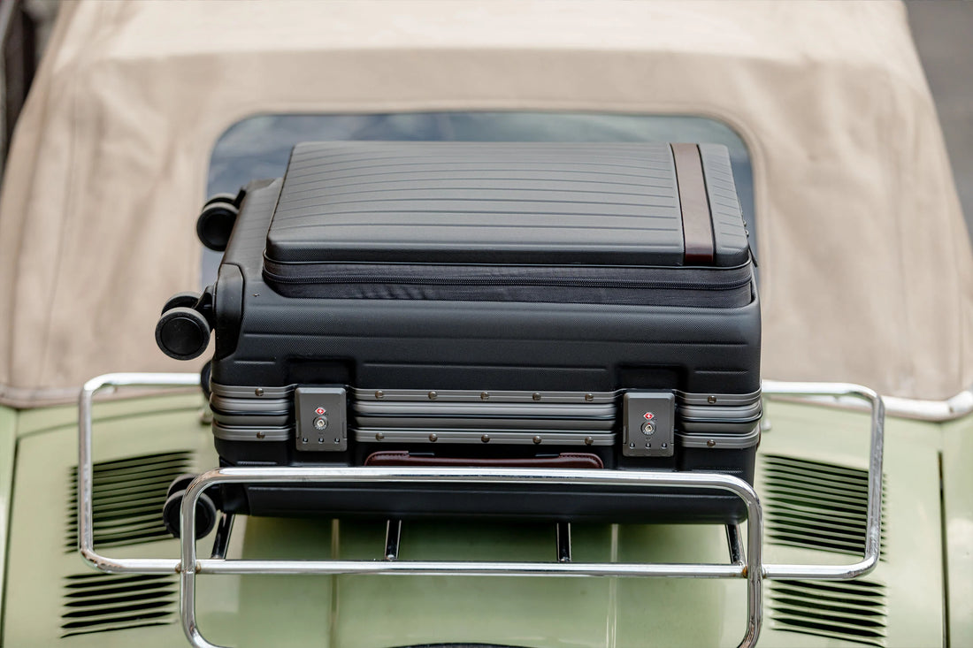 A black suitcase secured on the luggage rack of a vintage car.