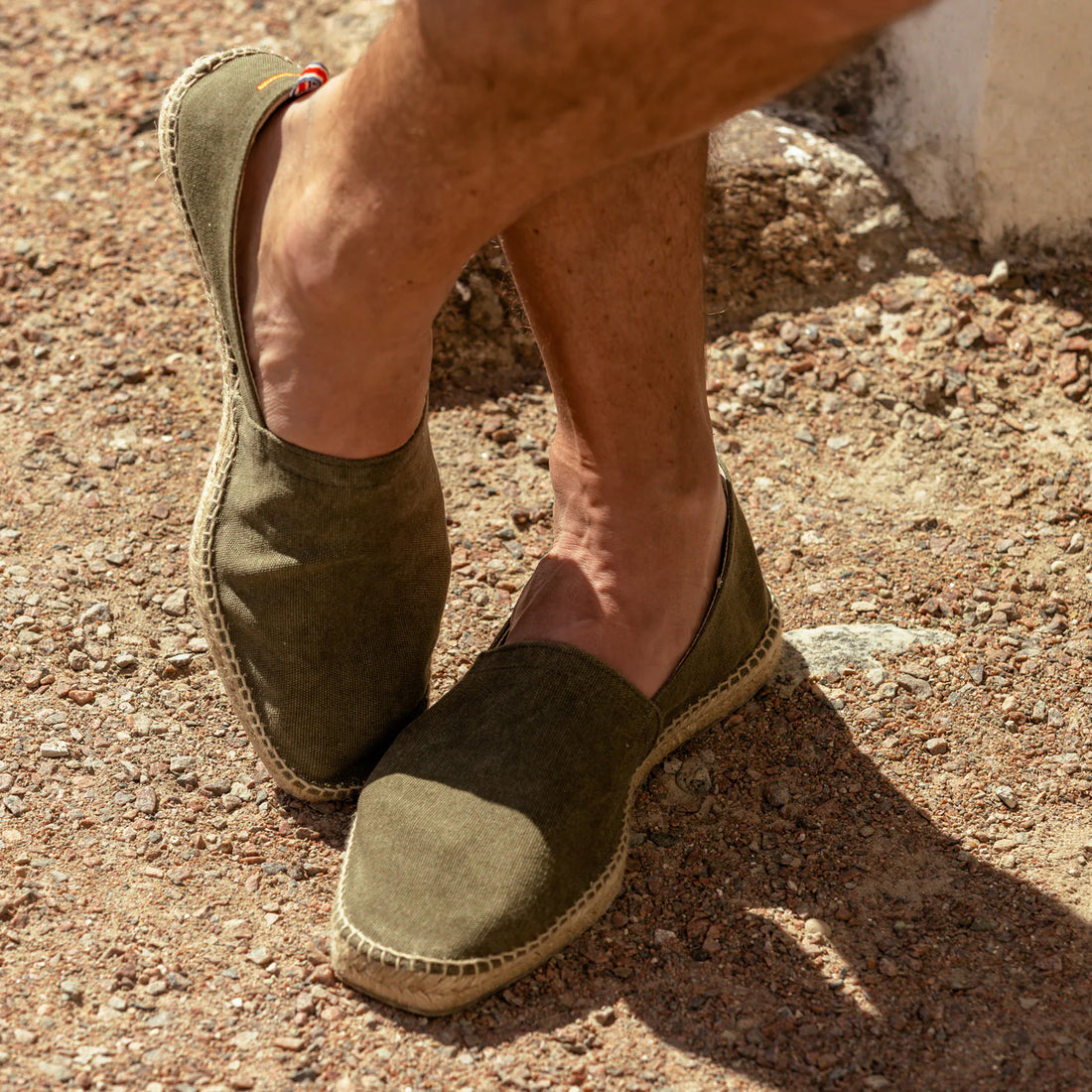 A person wearing green espadrilles standing on a gravel surface.