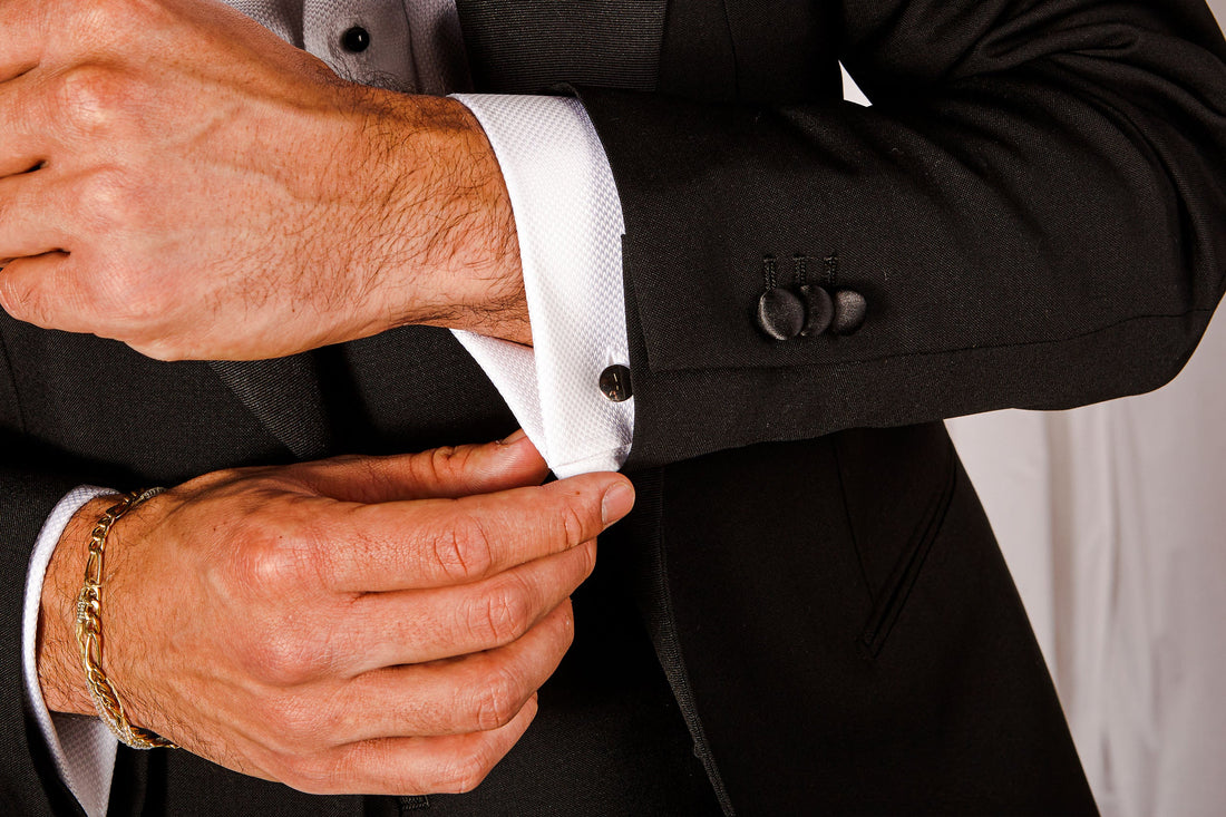 A person in a black suit fastening cufflinks on a white dress shirt sleeve.