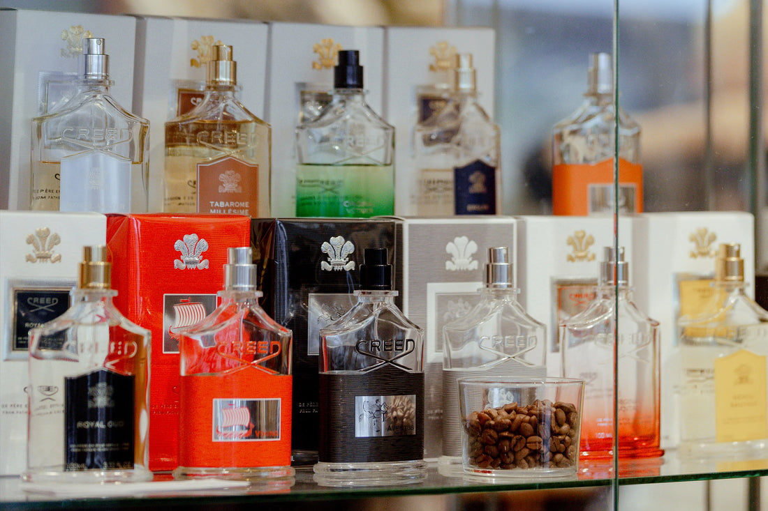 A collection of various designer perfume bottles displayed on glass shelves.