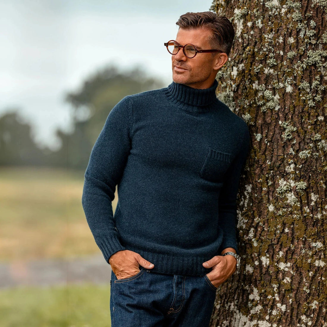 Man in glasses leaning against a tree outdoors.