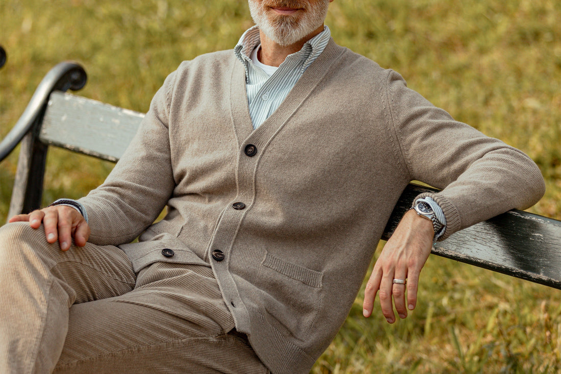 Mature man in a stylish cardigan and trousers sitting relaxed on a park bench.