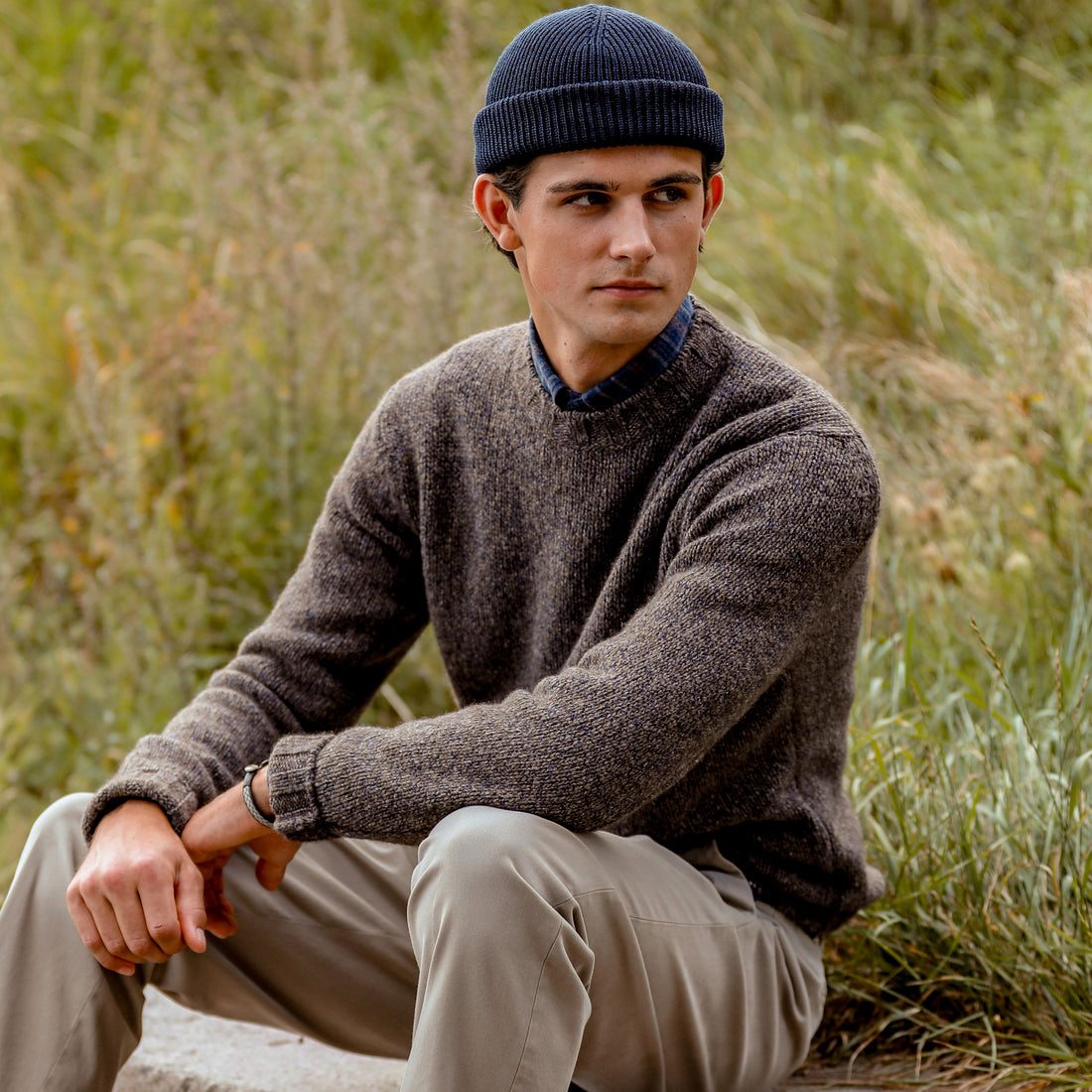 Mature man in a stylish cardigan and trousers sitting relaxed on a park bench.