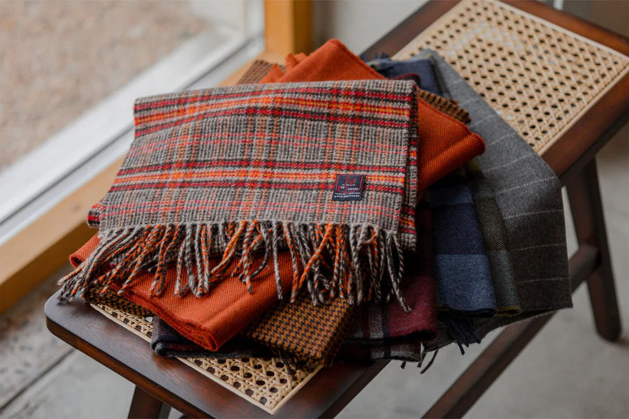 A stack of folded tartan scarves on a wooden chair.