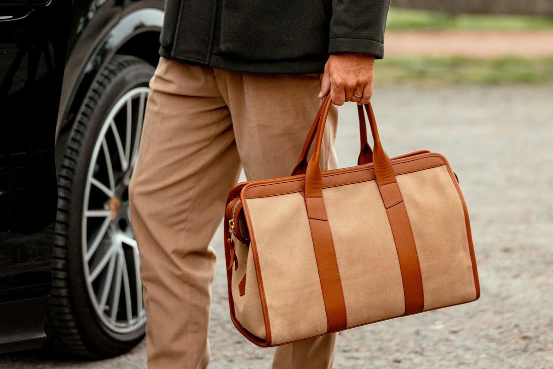 Person holding a brown leather bag next to a car.