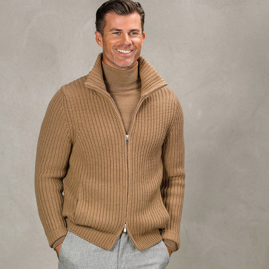 Man wearing a beige zip-up sweater over a white shirt.