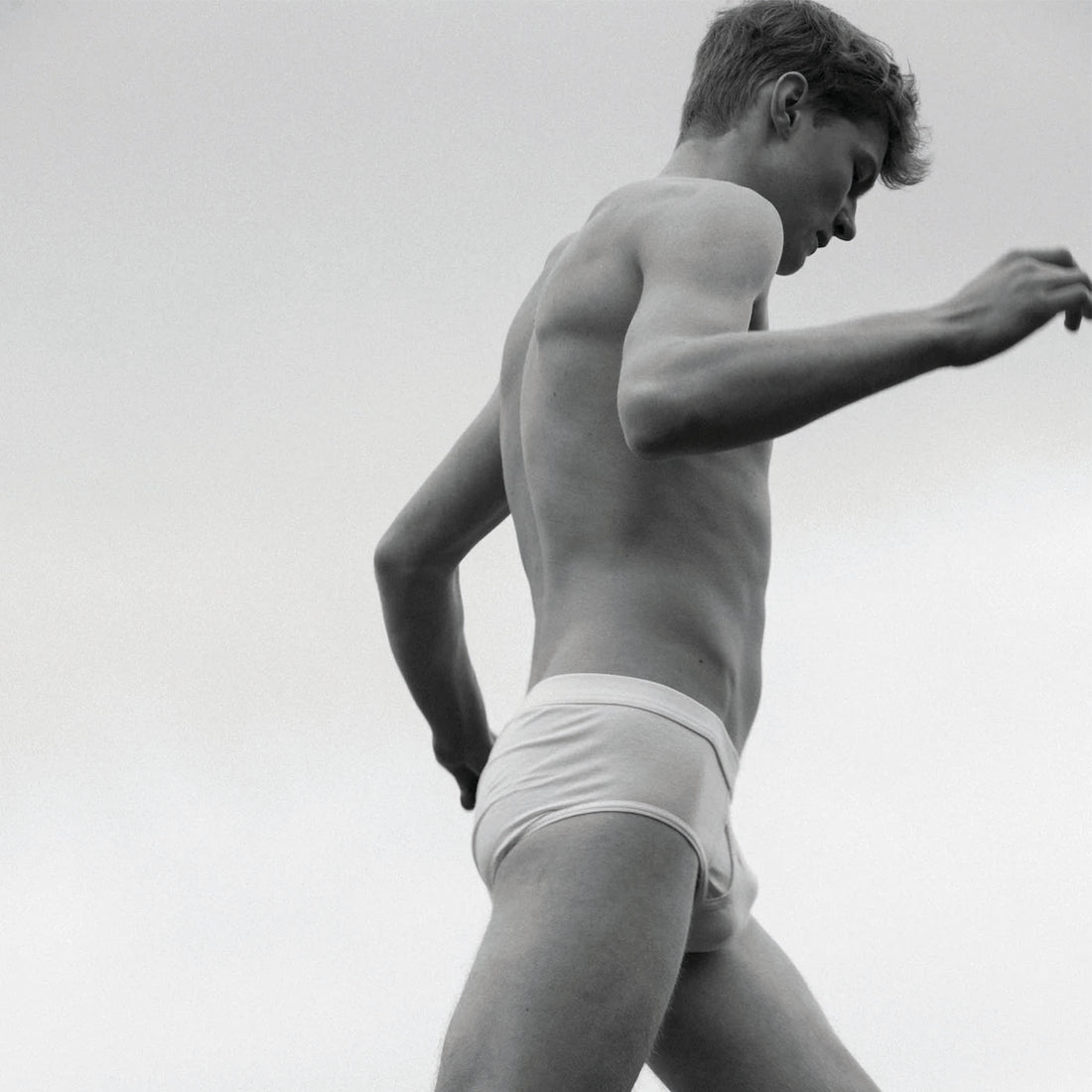 Black and white image of a person wearing white underwear, captured from a low angle against a cloudy sky background.