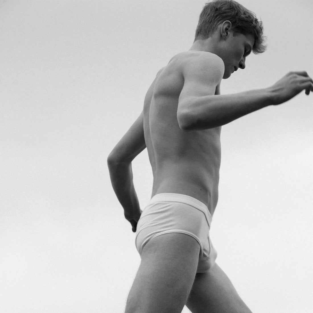 Person in white underwear is captured in a low-angle shot, seemingly in motion against a cloudy sky background.