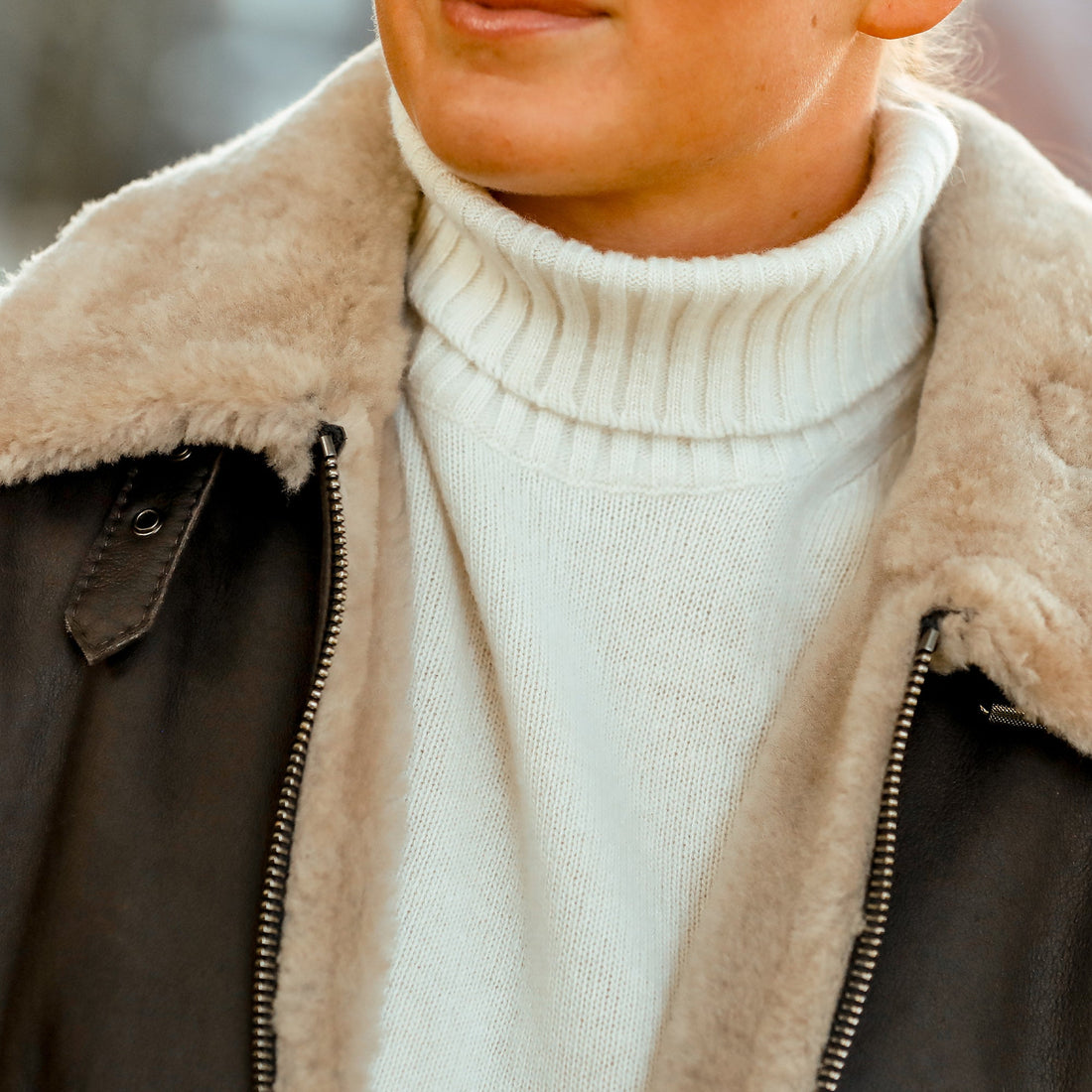 Person wearing a shearling jacket over a white turtleneck sweater.