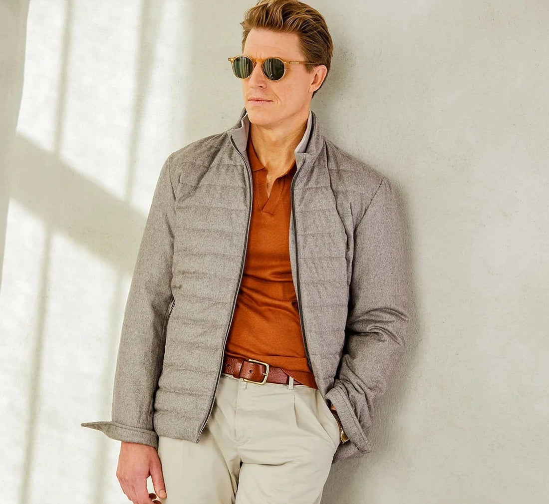Man in smart casual wear with sunglasses leaning against a wall.