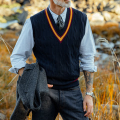 A person wearing an Alan Paine Navy Blue Striped Merino Wool Cricket Slipover over a striped shirt with a tie stands outdoors holding a gray jacket.