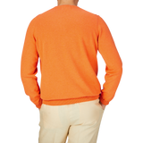 A person seen from behind wearing an Blazing Orange Luxury Cotton Crewneck by Alan Paine and beige pants against a blue background.