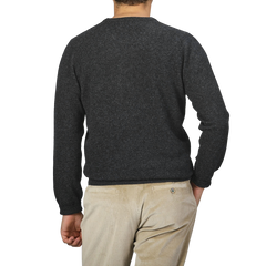 An individual is depicted from behind, dressed in the Charcoal Grey Lambswool Crew Neck by Alan Paine, paired with light-colored corduroy pants, against a plain backdrop.