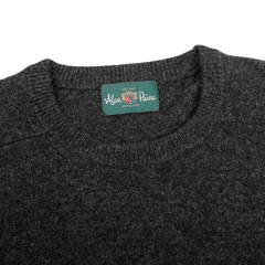 A close-up of the Charcoal Grey Lambswool Crew Neck sweater from Alan Paine, featuring a green label that reads "Alan Paine, England," made from the finest Australian lambswool.