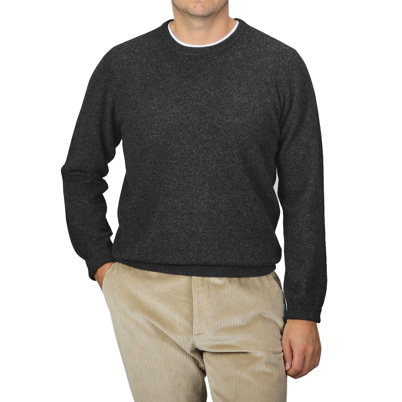 A man is wearing an Alan Paine Charcoal Grey Lambswool Crew Neck sweater along with light brown corduroy pants, standing against a plain gray background with his right hand in his pocket.