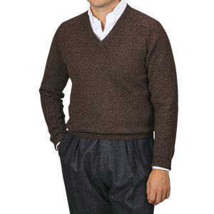 A person wearing an Alan Paine Cocoa Brown Lambswool V-Neck sweater over a white collared shirt with gray trousers, standing against a plain background.