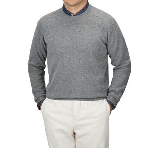 A person wearing an Alan Paine Grey Melange Lambswool Crew Neck over a blue collared shirt and beige pants, standing with hands in pockets against a plain background.