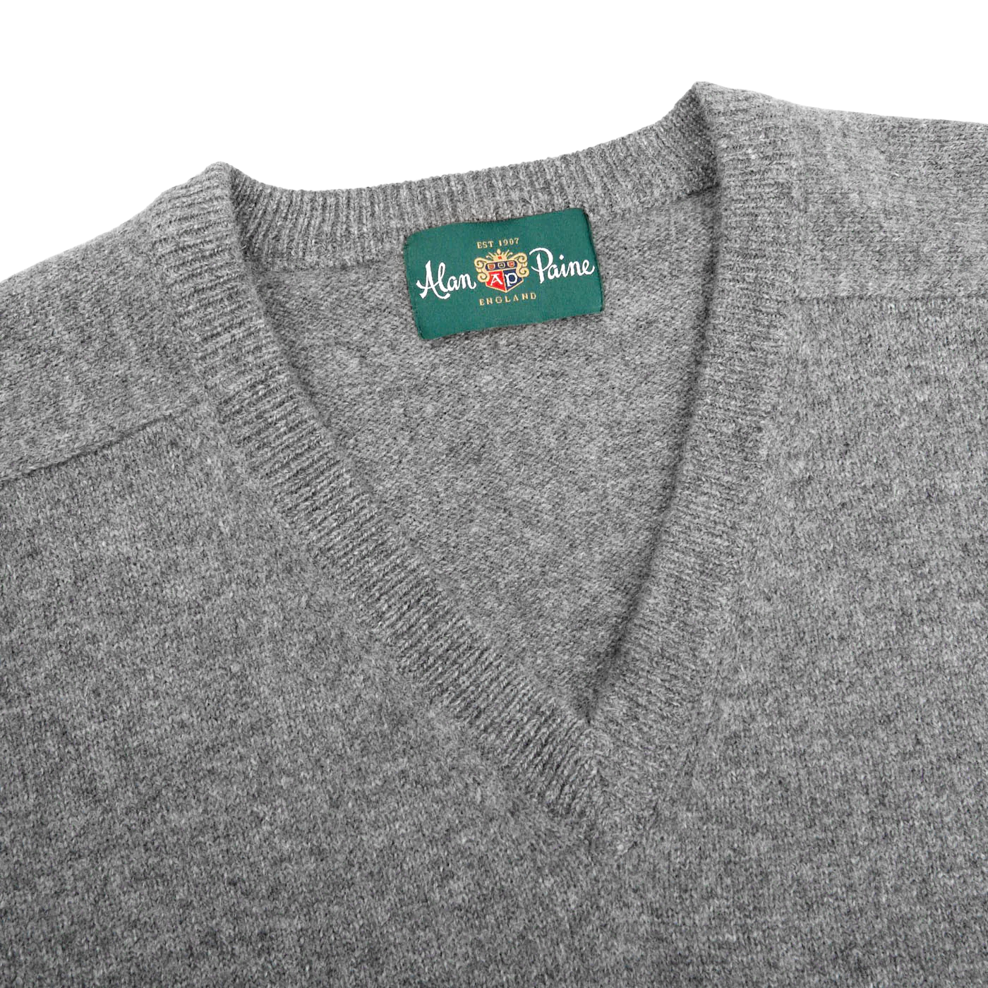 A close-up of a Grey Melange Lambswool V-Neck sweater by Alan Paine, crafted from luxurious Australian lambswool, with a green label showcasing the brand name.