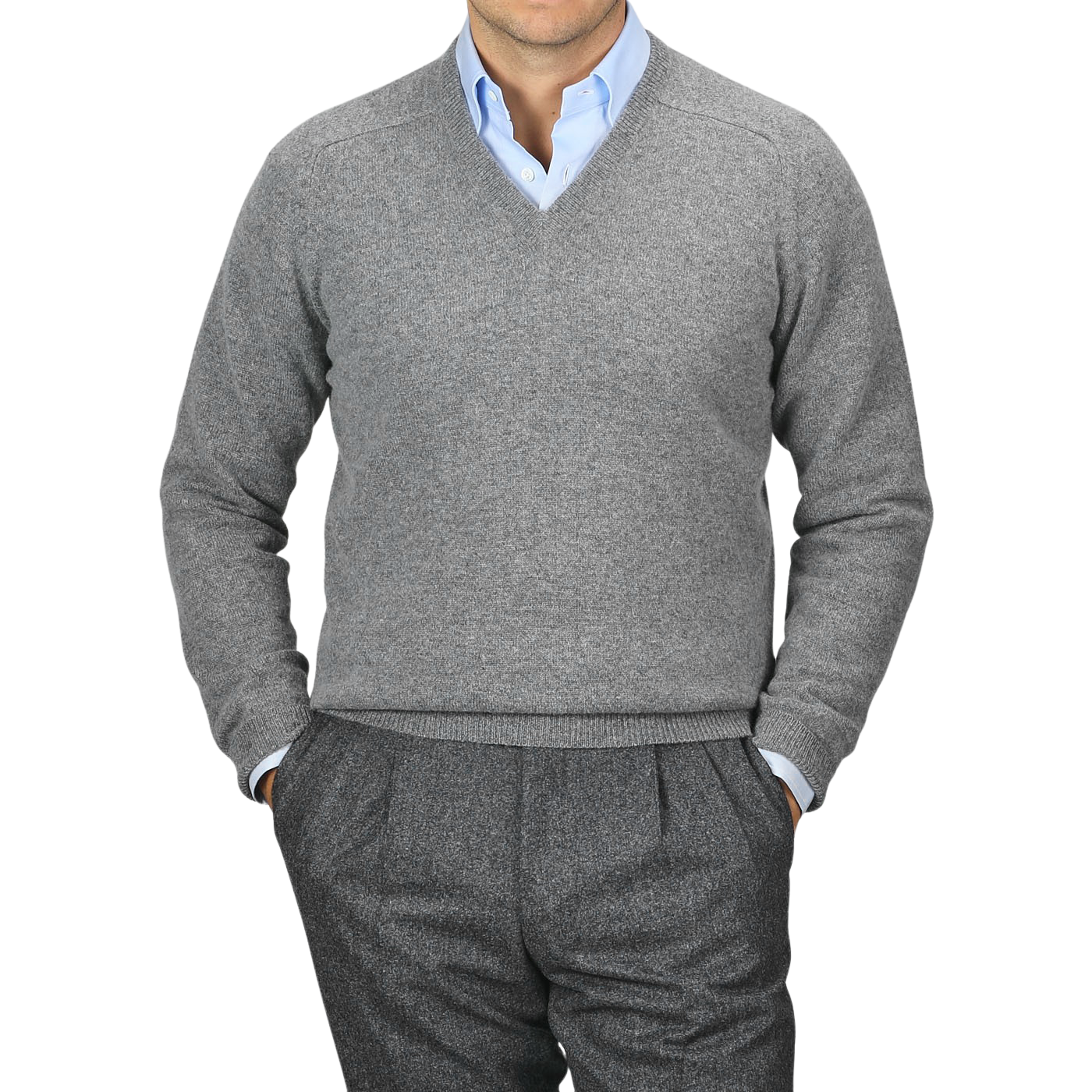 A person wearing an Alan Paine Grey Melange Lambswool V-Neck sweater over a light blue collared shirt, with hands in the pockets of grey pants. The background is plain and grey.