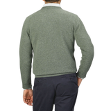 A person is seen from the back, wearing an Alan Paine Landscape Green Lambswool Crew Neck and dark-colored pants, with their right hand in their pocket.