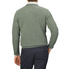 A person is seen from the back, wearing an Alan Paine Landscape Green Lambswool Crew Neck and dark-colored pants, with their right hand in their pocket.