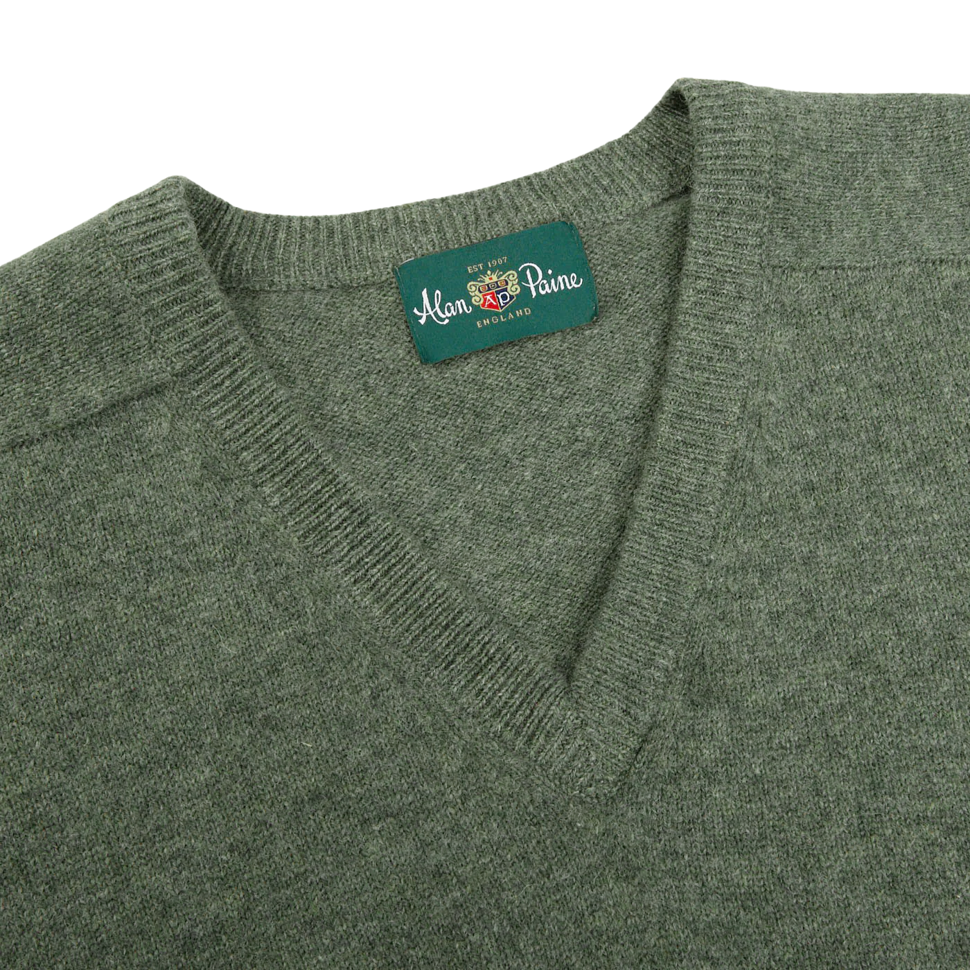 A close-up of the Landscape Green Lambswool V-Neck sweater, made from luxurious Australian lambswool and featuring a tag that reads "Alan Paine, England.