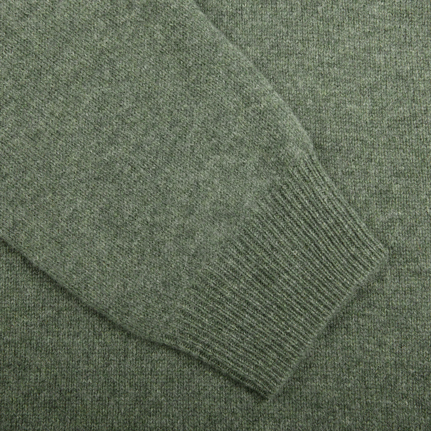 Close-up image of a textured, green knitted fabric, likely a Landscape Green Lambswool V-Neck sweater sleeve from Alan Paine extending diagonally across the frame. The cuff appears ribbed, contrasting with the smoother body of the garment.