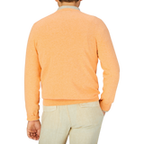 A person wearing an Alan Paine mango orange luxury cotton v-neck sweater and cream-colored pants standing with their back to the camera.
