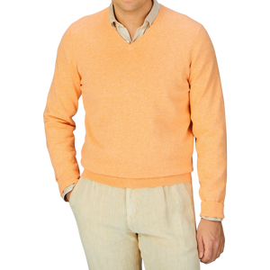 Man wearing an Alan Paine mango orange luxury cotton v-neck sweater over a light shirt with beige pants.