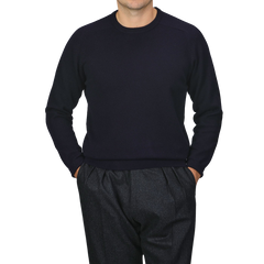 A person wearing an Alan Paine Navy Blue Lambswool Crew Neck sweater and dark gray trousers, with hands in pockets, standing against a plain gray background.