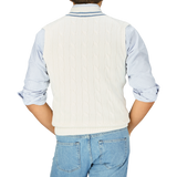 Person wearing an Off-White Blue Striped Cotton Cricket Slipover by Alan Paine over a blue and white striped shirt, paired with denim jeans, viewed from the back.